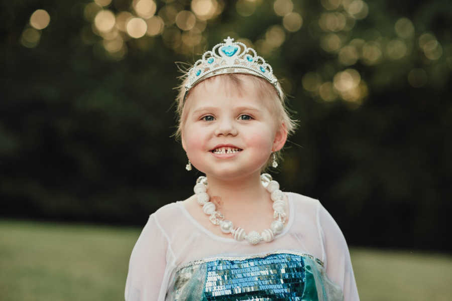 Little girl with leukemia wearing a princess dress and crown smiling