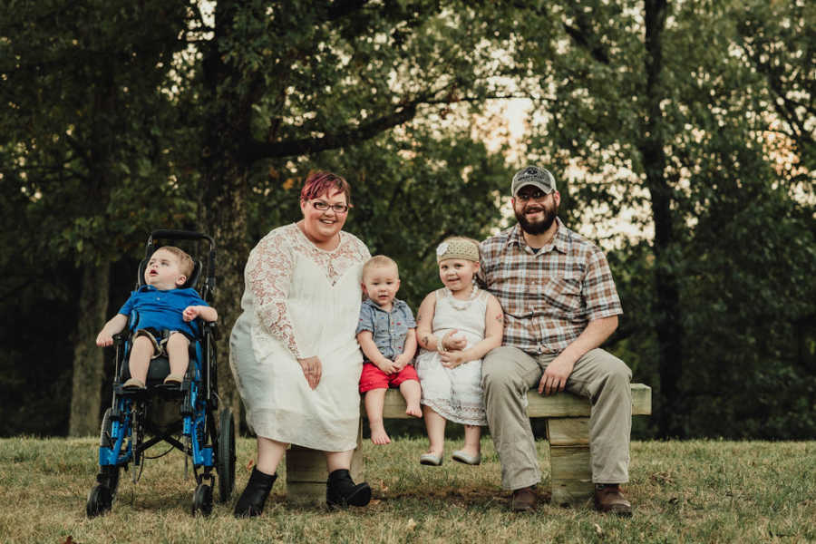 Husband and wife sit on either side of bench next to daughter with leukemia, youngest son, and middle child with brain injury