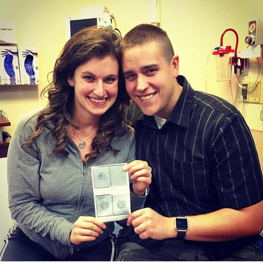 Husband and wife sit smiling holding up sonogram of three eggs that reached embryo stage