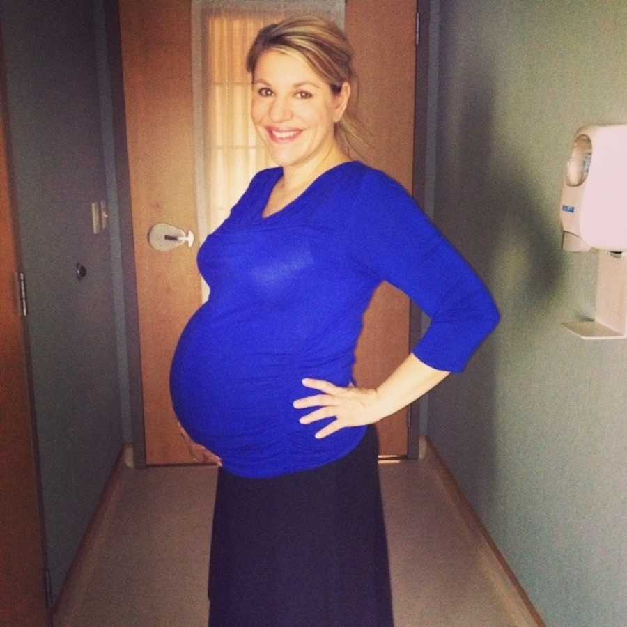 Pregnant woman stands smiling with hands on her hips