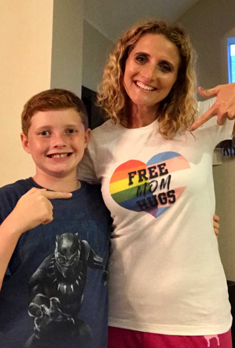 Mother smiles beside her trans child pointing to her shirt that says, "Free mom hugs"