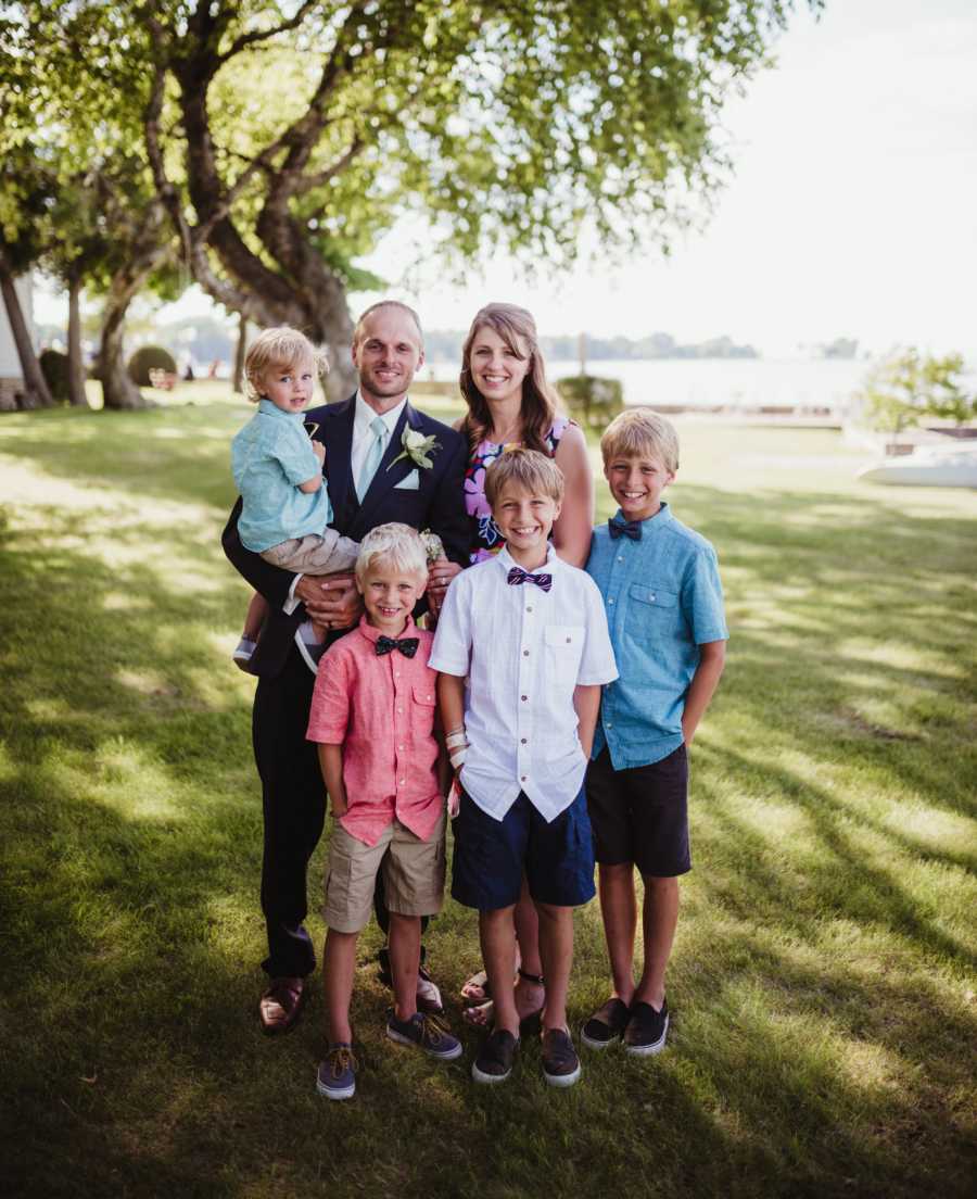 Man stands holding youngest son beside three other sons and wife who has since passed away