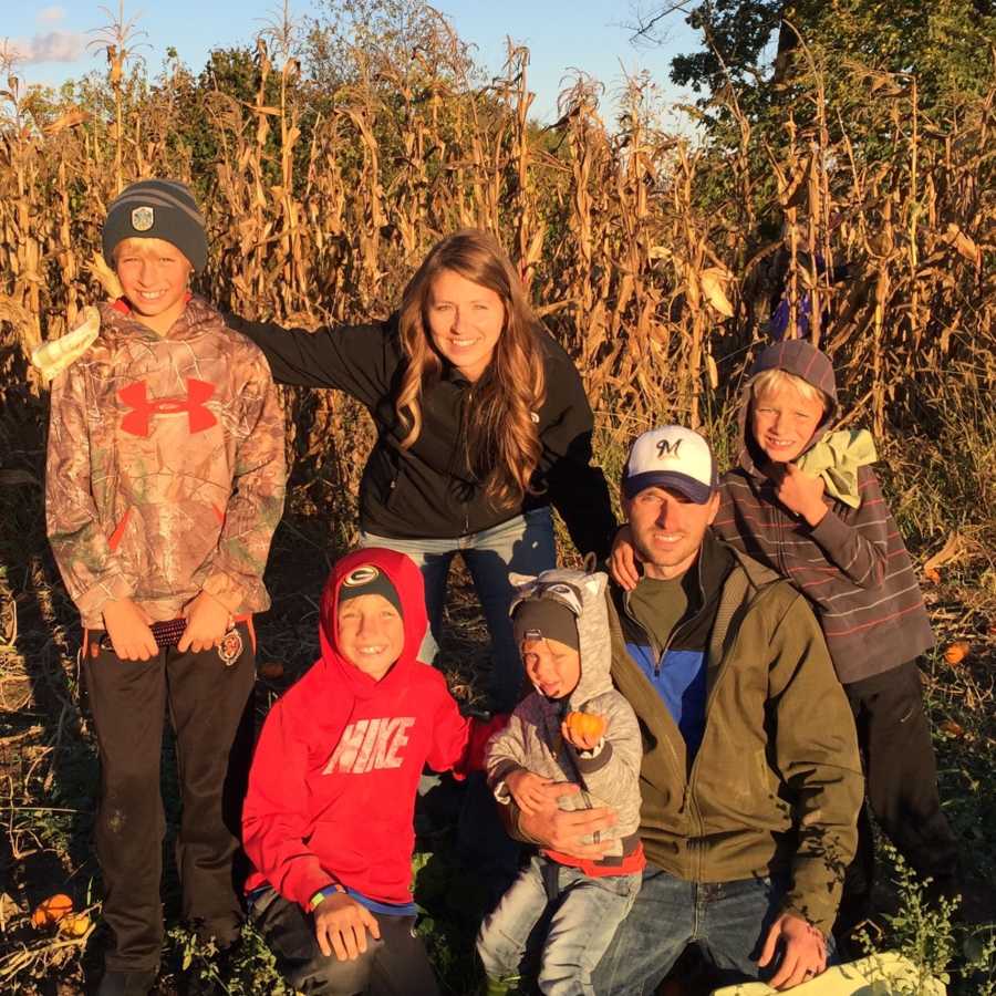Man squats in corn field with younger son in his arms beside other three sons and wife who has since passed