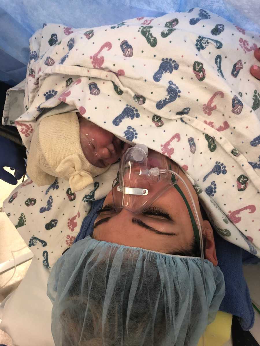 Mother who struggled with fertility lays in hospital bed with oxygen mask holding newborn