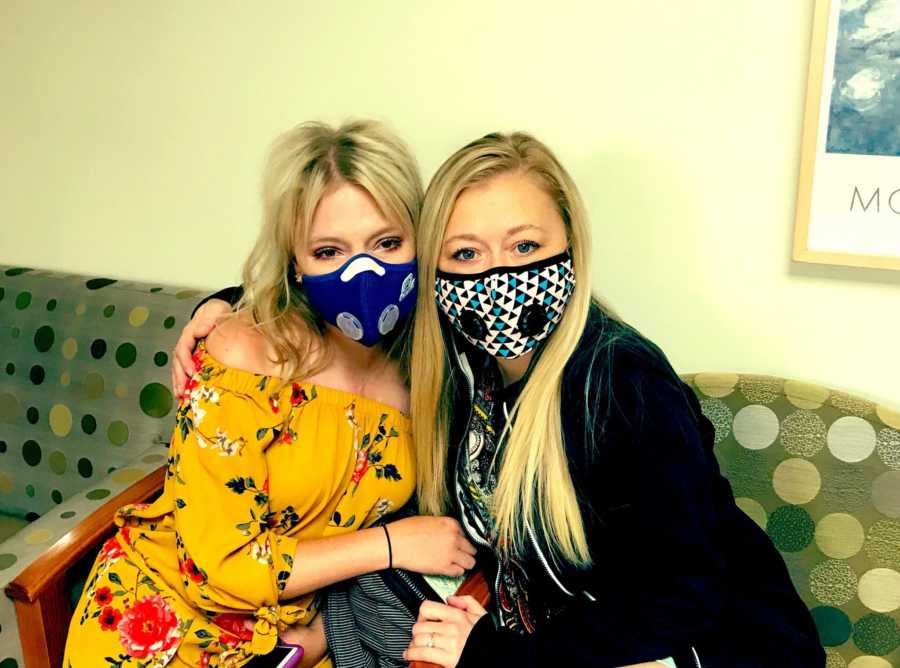 Woman with Cystic Fibrosis sits with mask on in doctor's office with arm around another woman