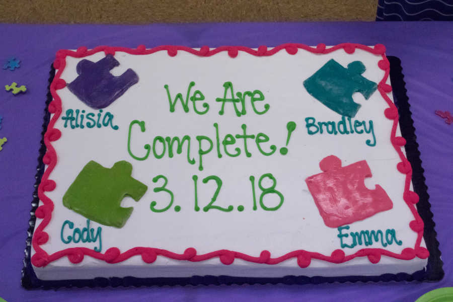 Cake that says, "We are Complete 3.12.18" with names of four children who were adopted by foster parents