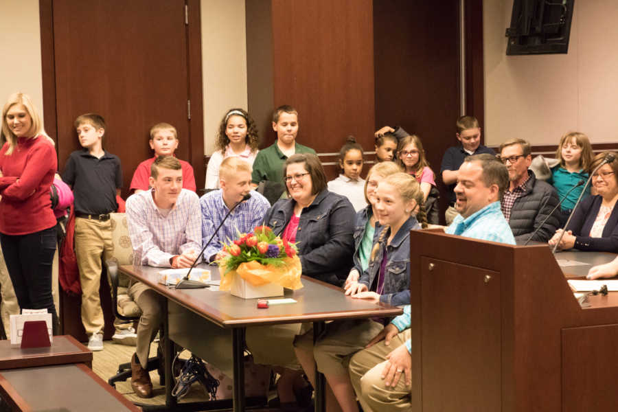 Foster mother and father sit at table in adoption court with four foster children 