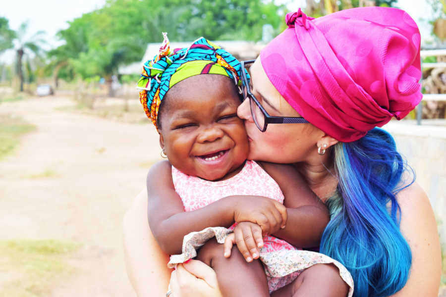 Mother holds and kisses adopted daughter on the cheek who is smiling