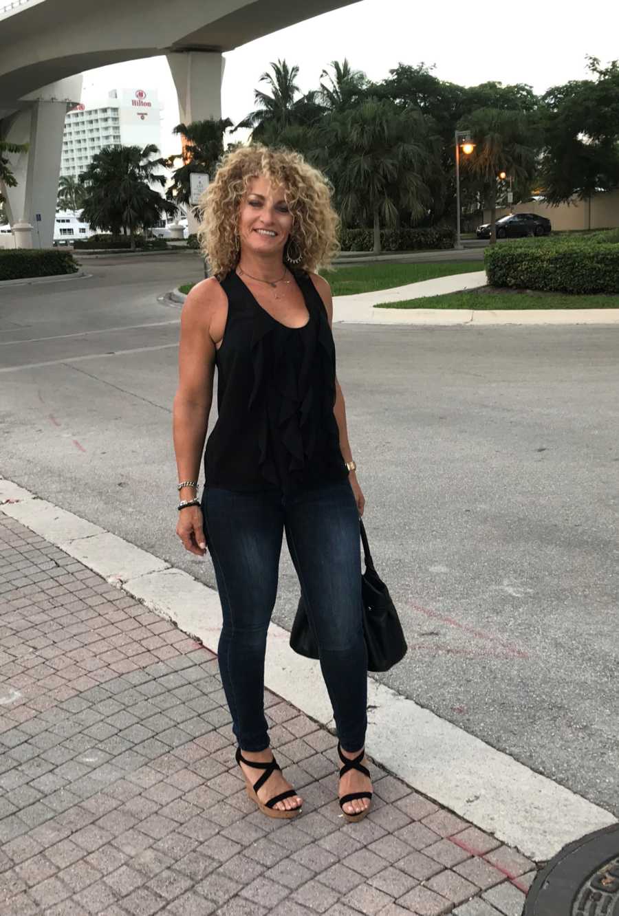Woman who became sober stands smiling in cross walk holding purse
