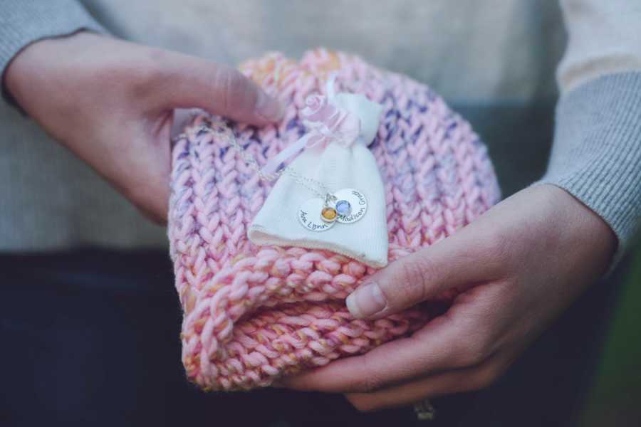 Mother holds pink knit hat that has necklaces laying on it that represents her two daughters that have passed