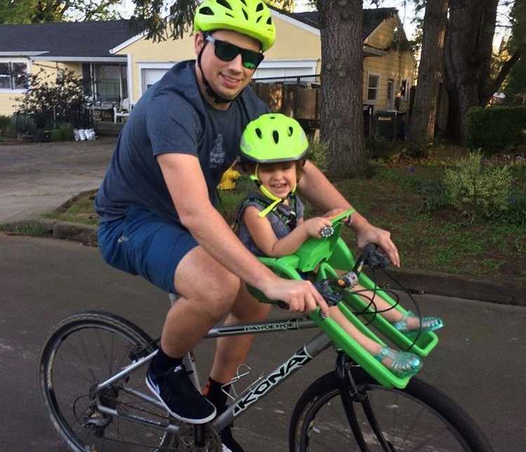 Man with bone marrow disease smiles while riding bike with daughter sitting in seat attached to handle bars