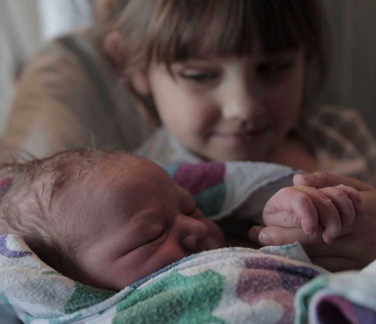 Close up of newborn being held by toddler sister whose father passed away before birth of newborn