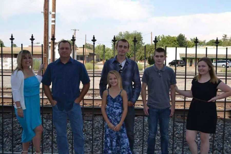 Woman stands holding onto fence besides deceased husband and four children