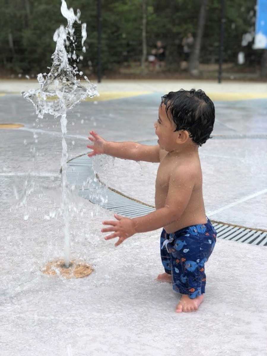 Adopted child with undiagnosed disease stands beside water fountain at water park