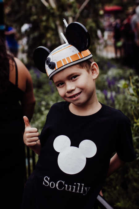 Little boy who had citrus burn stands with thumbs up smiling at Disney Land with mickey mouse ears on