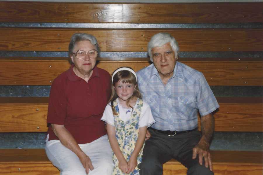 Little girl sitting between her grandparents on wooden bleachers