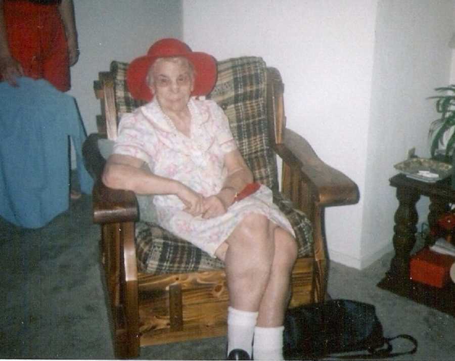Elderly woman sitting in chair wearing dress and red hat