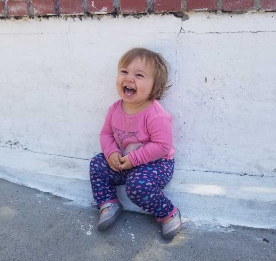 Toddler smiles while sitting on ledge outside whose mother had her after losing first child