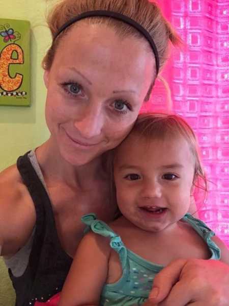 Mother with anxiety smiles in selfie with her toddler daughter