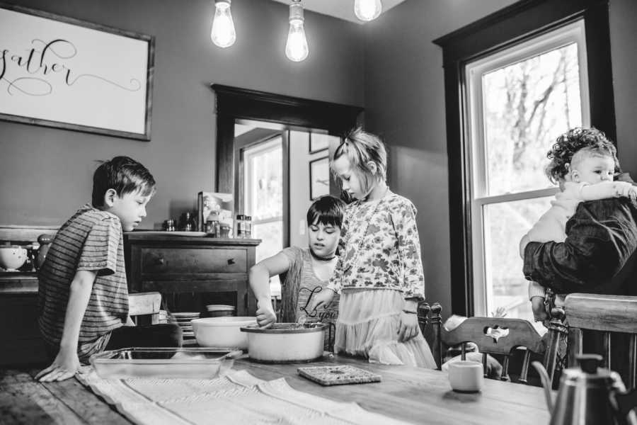 Three foster children sit at dining room table watching one mixing something in bowl