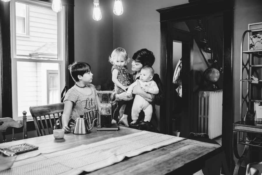 Single foster mother holding two children in her arms looking at young boy in dining room