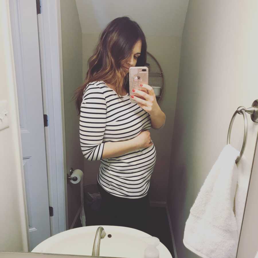 Woman who went through IVF treatments takes mirror selfie in bathroom holding stomach