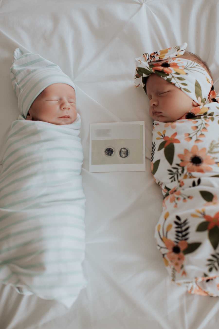 Newborn twins lay swaddled in blankets with the picture of their successful embryo transplant between them