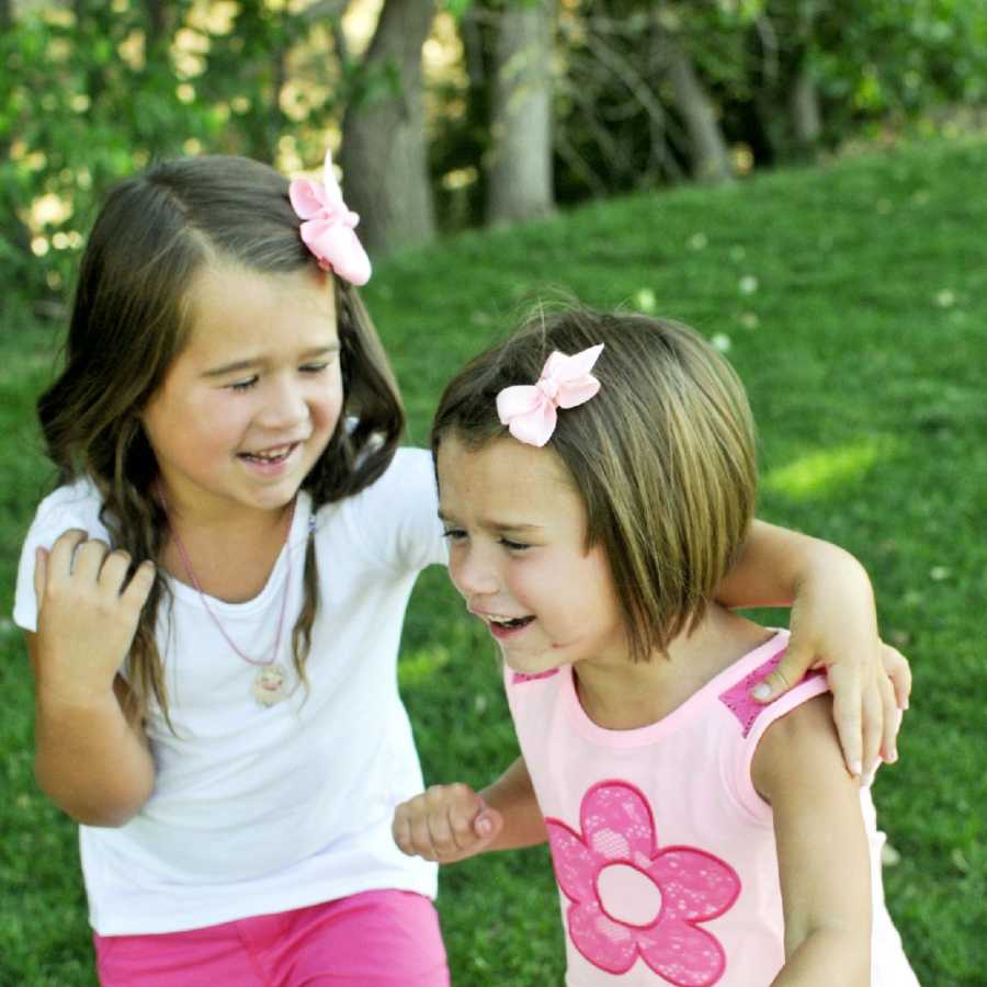 Toddler with shaken child syndrome stands with older sister outside laughing