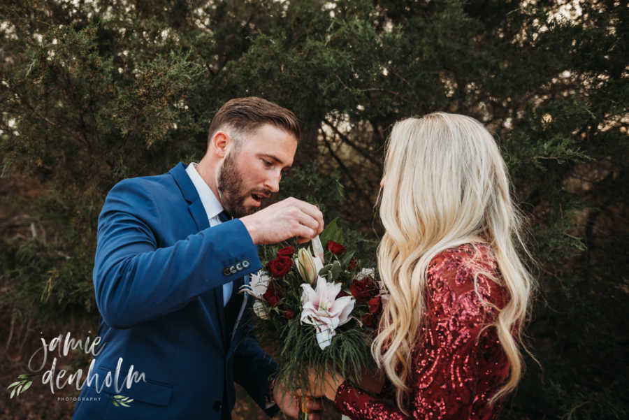 Wife holds out bouquet of flowers to husband as he pulls something out of bouquet