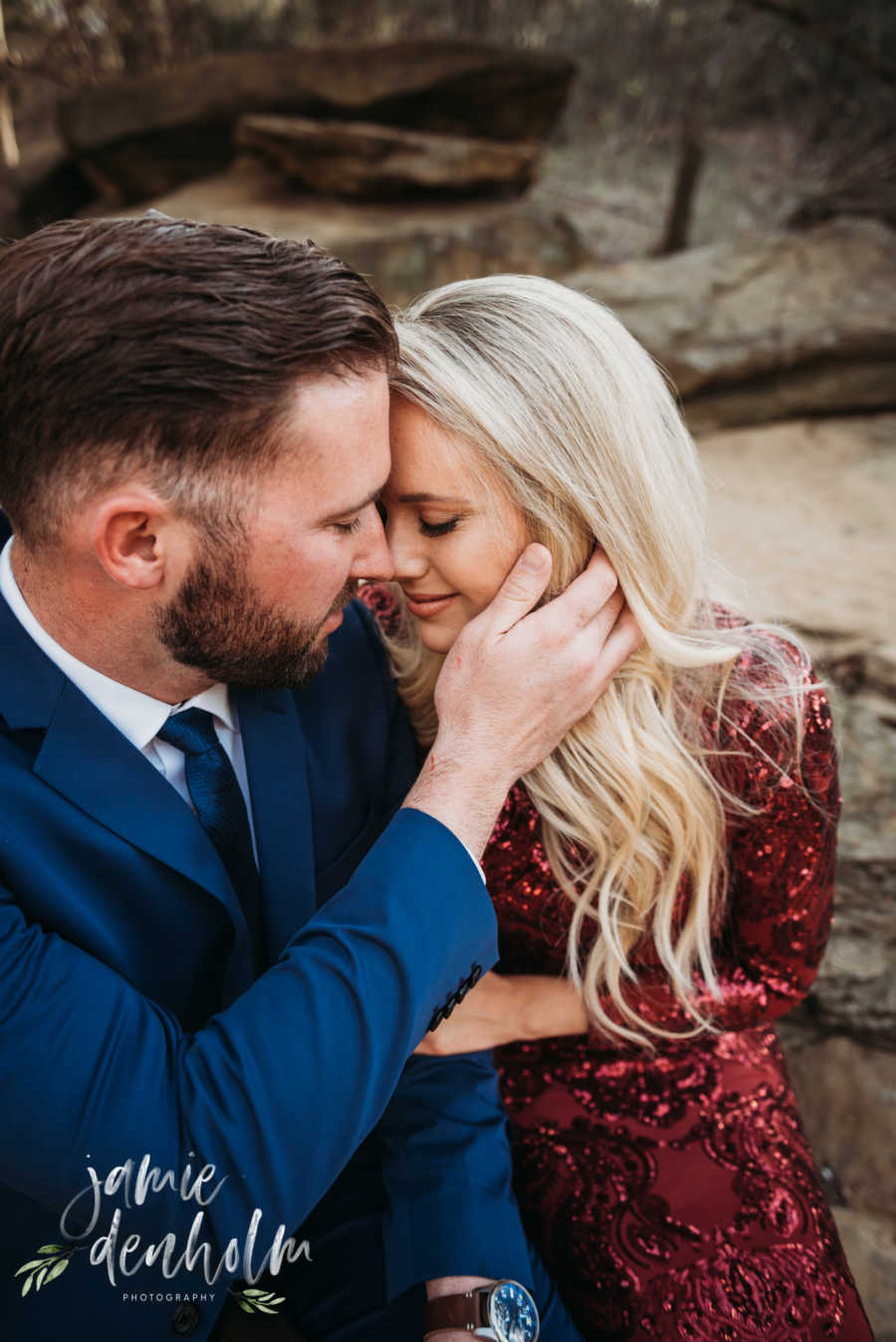 Husband sits beside wife holding her face as their foreheads touch