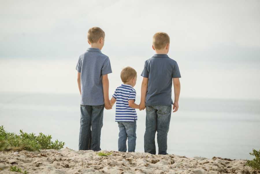 Young boys stand on either side of their cousin holding his hand 
