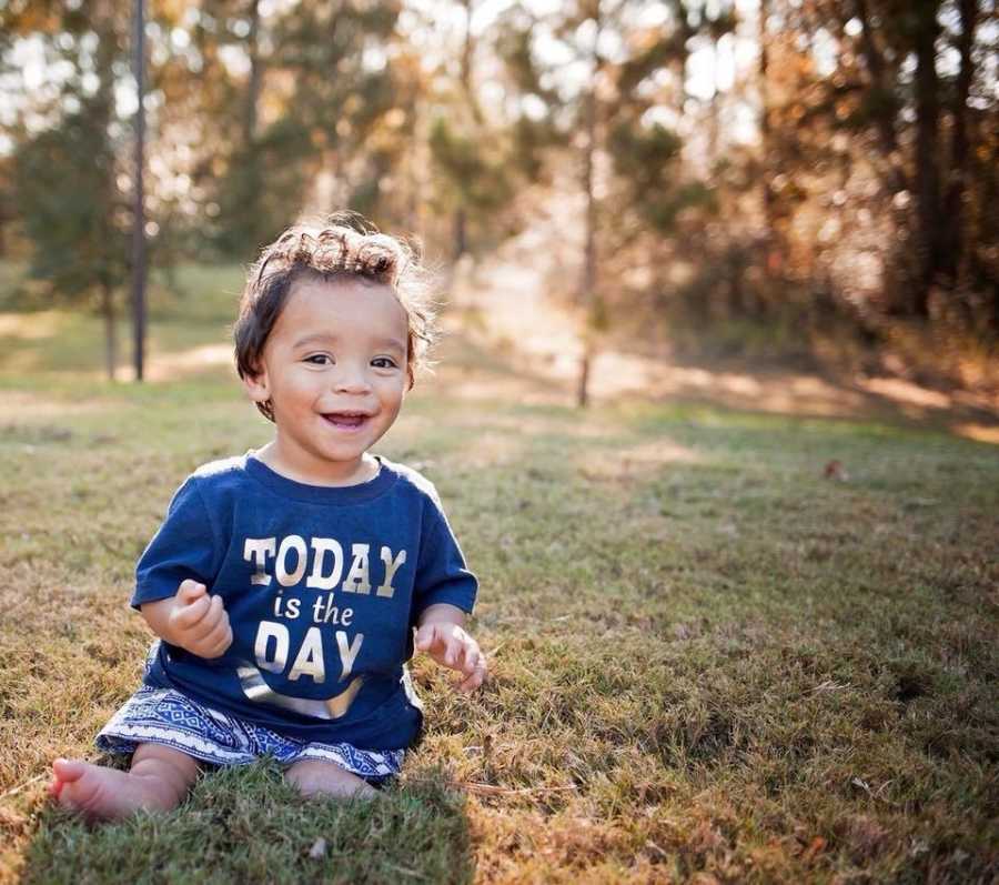 Foster child with unknown issues sits smiling in grass wearing shirt that says, "Today is the Day"