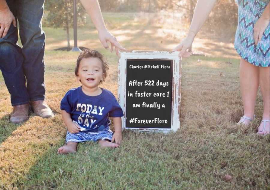 Foster parents hold sign next to toddler that says, "After 522 days in foster care I am finally and #ForeverFloro"