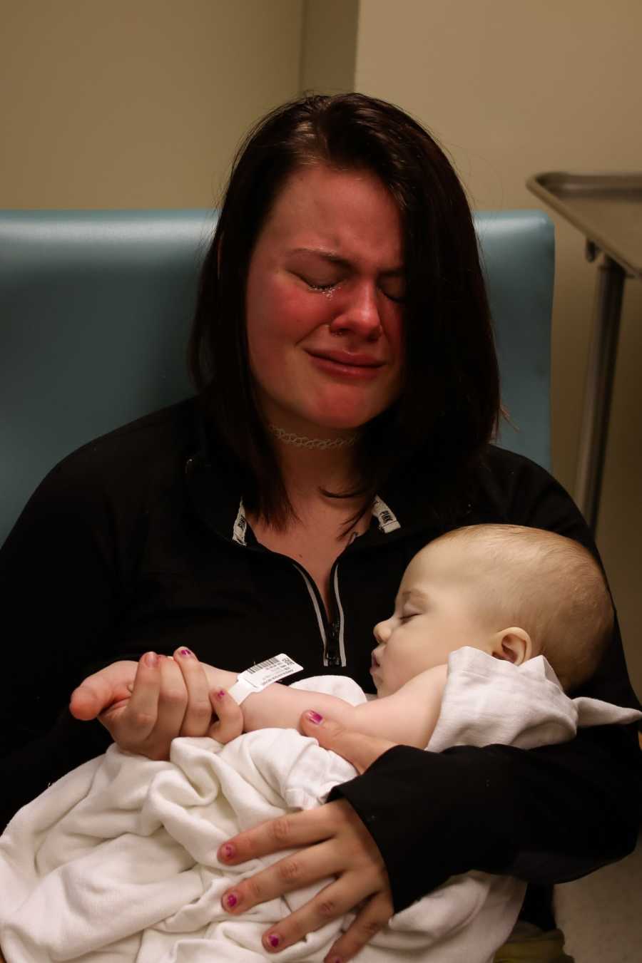 Mother sits in chair sobbing as she holds 8 month old deceased son