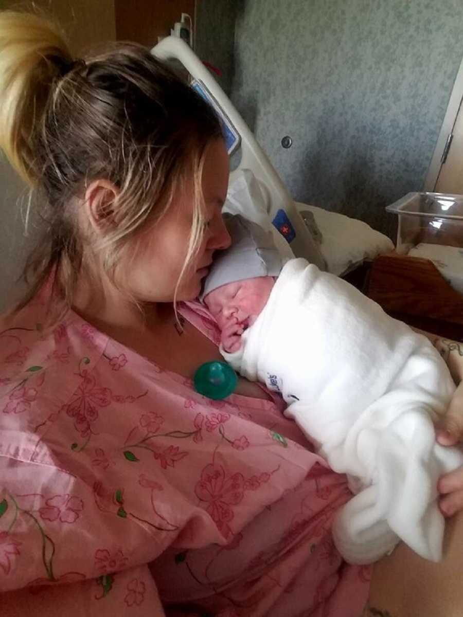 Mother who just gave birth rests head on newborn's head who is sleeping on her chest