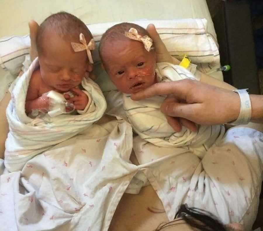 Newborn twins swaddled in blankets with light pink bows in their hair