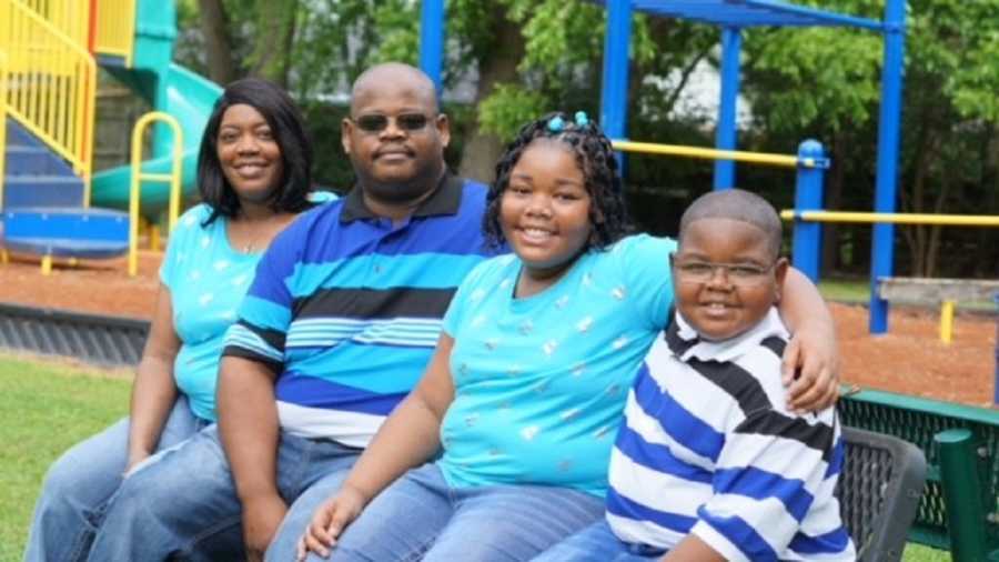 Woman whose first child was a still born sits on bench at playground beside husband and two children