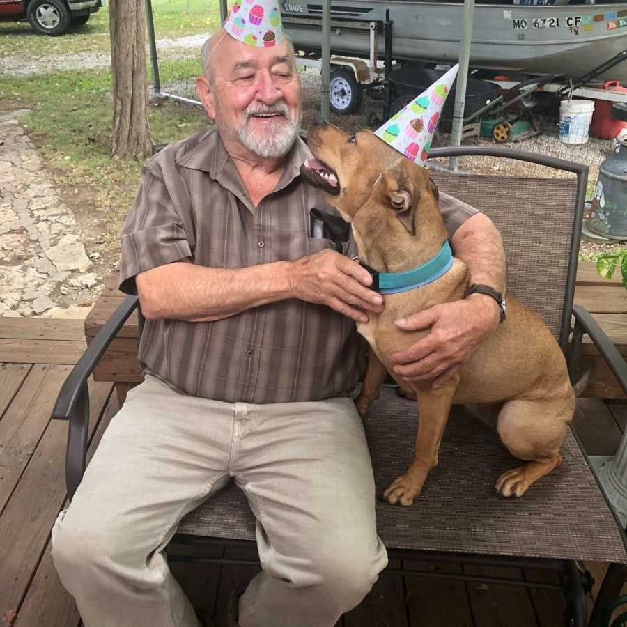 80 year old man smiles at adopted dog that is sitting next to him on outdoor chair
