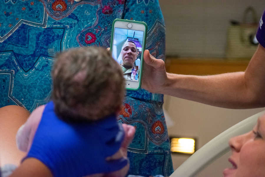 iPhone is held up on facetime so military husband can see newborn child