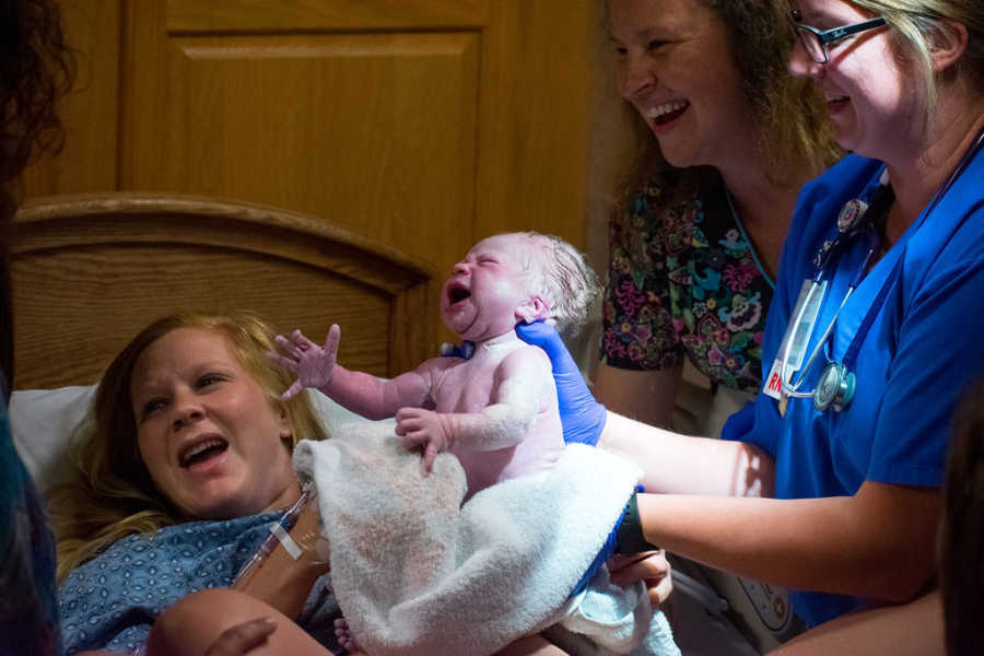 Woman smiles as nurse holds up newborn