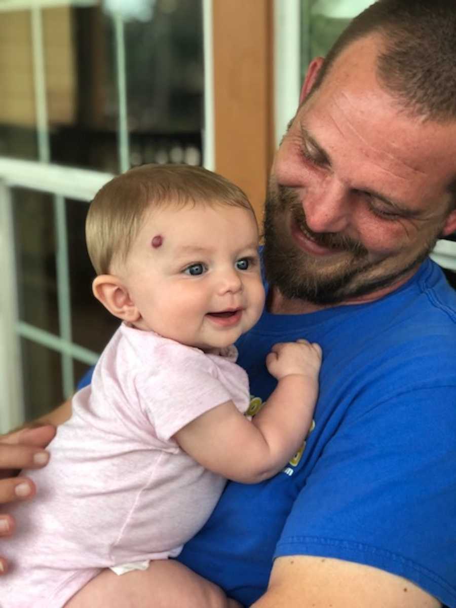 Father smiles while holding and smiling toddler daughter