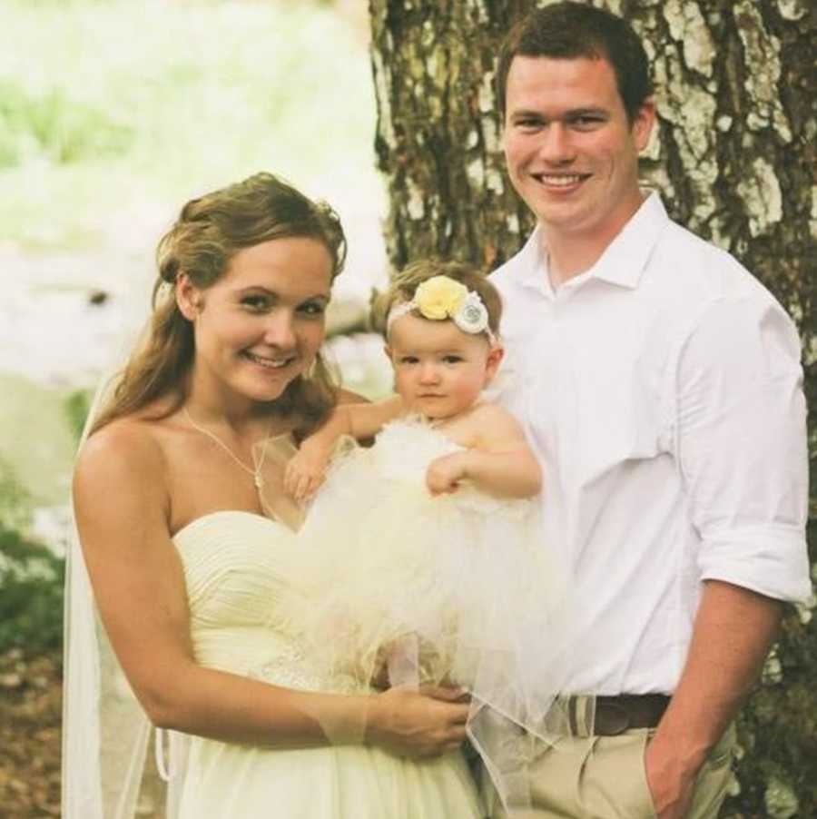 Bride holding her baby beside groom on wedding day