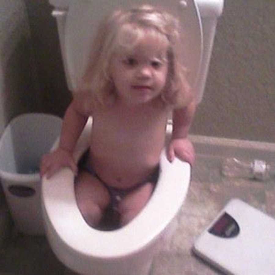 Little girl of single parent sits in toilet bowl
