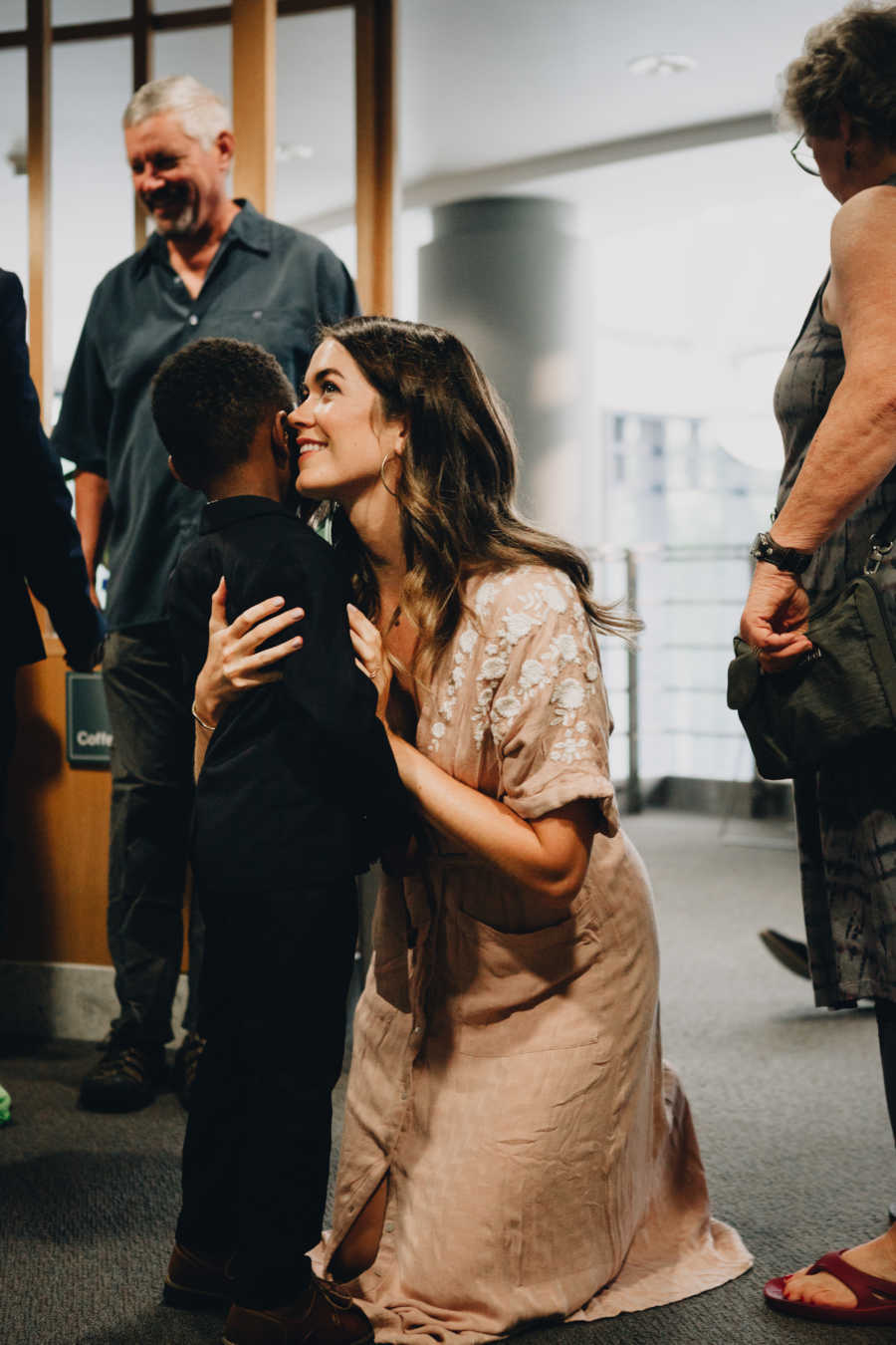 Woman rests on knees giving son she just adopted a hug 