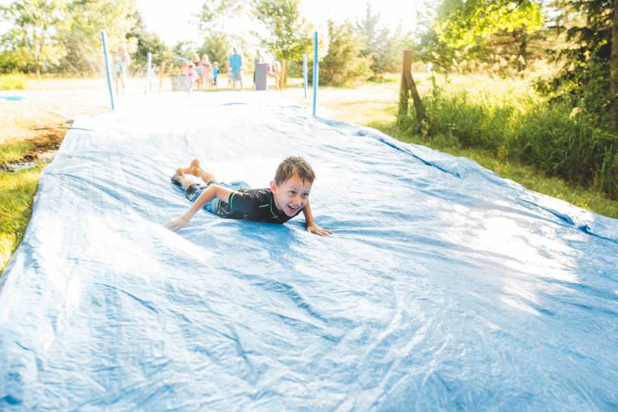 Young boy in foster care slides down slip and slide