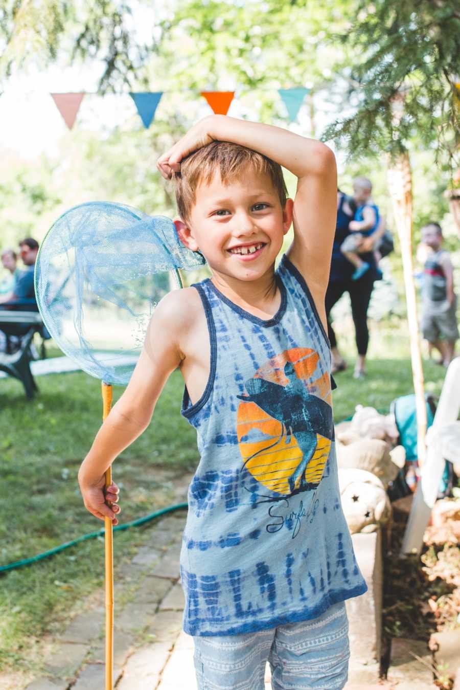 Young foster child smiles with arm resting on his head and fishing net in hand