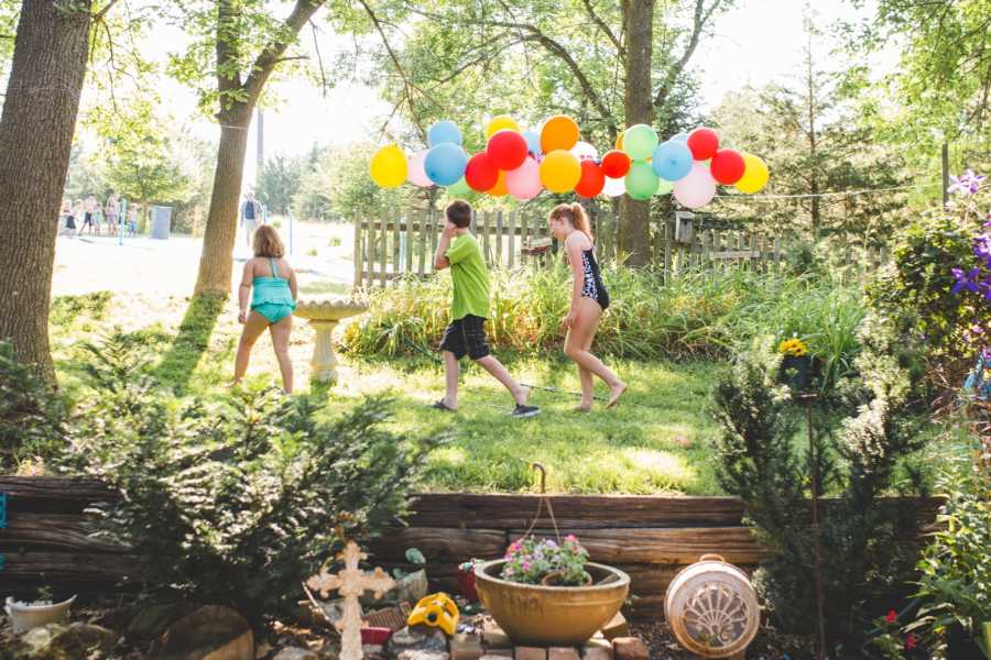 Kids in swimsuits walking in yard with colorful balloons