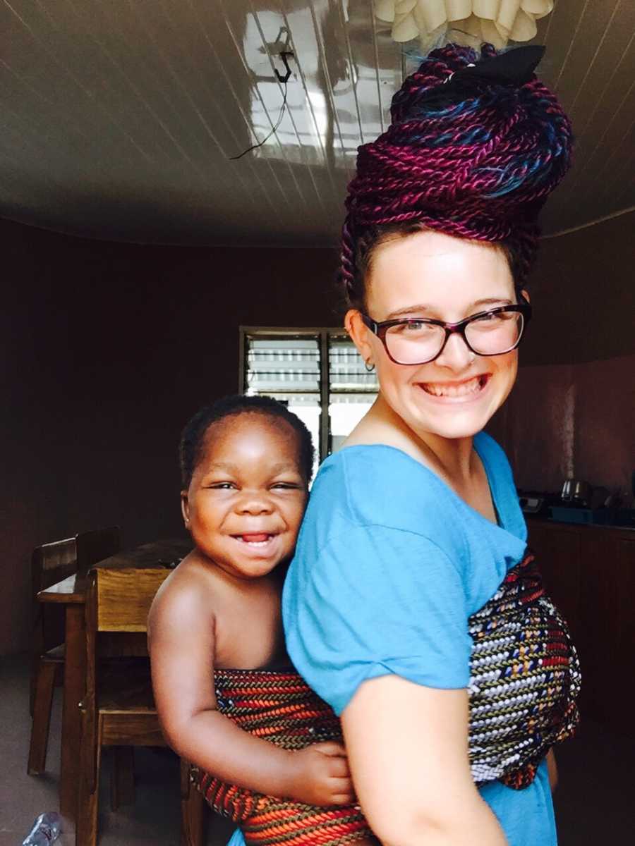 Mother smiles with her adopted daughter from Africa swaddled to her back smiling