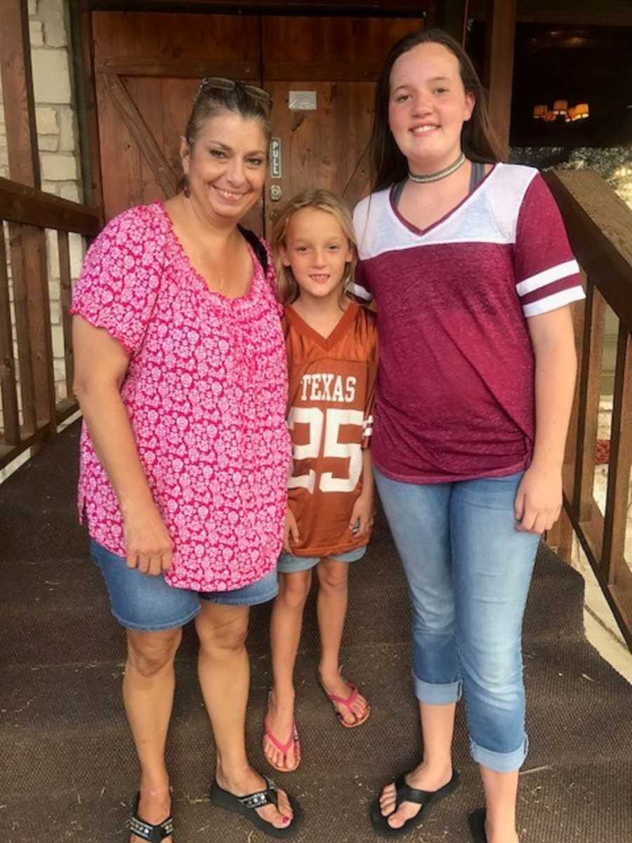 Woman who has struggled with drug abuse stands smiling with two granddaughters