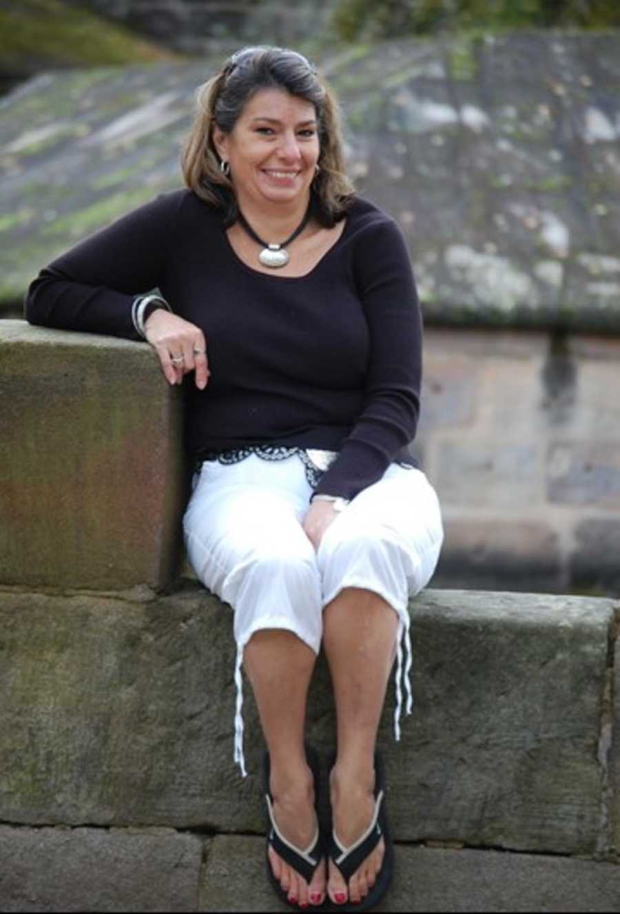 Woman who has since passed from drug abuse sits on stone wall smiling 